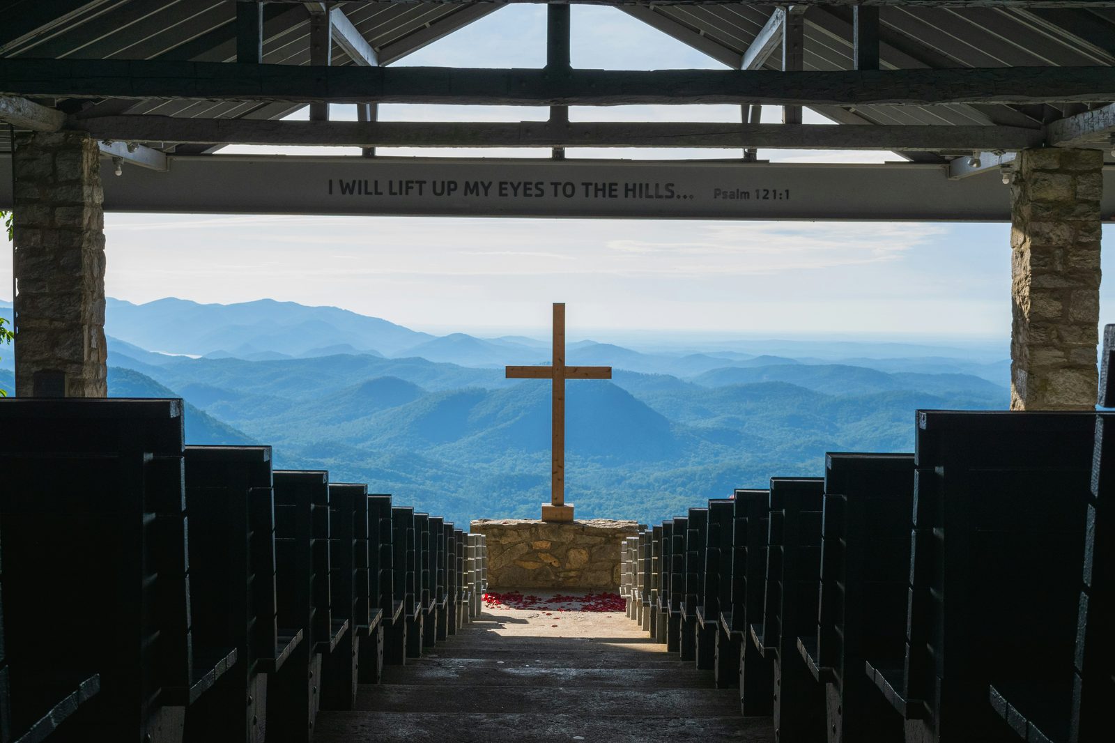 A wooden cross facing a wide mountain view from an open-air chapel